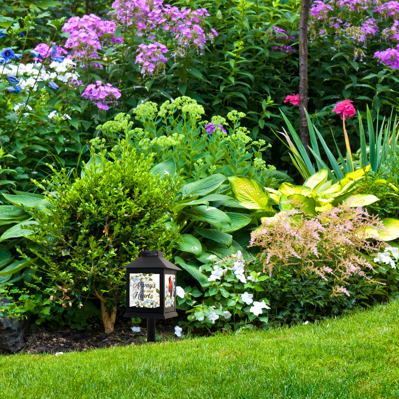 Garden scene with a decorative memorial cardinal garden light surrounded by various plants and flowers.